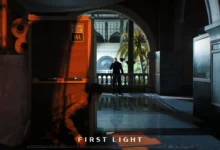 A person crouches behind shipping crates in a dimly lit museum, observing a man in a tuxedo who stands on a balcony overlooking a courtyard.