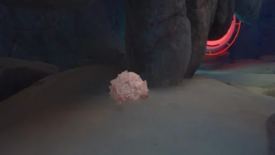 A cluster of pink crystals sits on a sandy surface inside a dark rocky cave with a glowing red portal in the background.