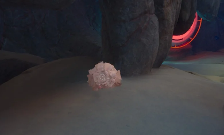 A cluster of pink crystals sits on a sandy surface inside a dark rocky cave with a glowing red portal in the background.