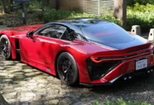A sleek red sports car with a black roof parked on a cobblestone path in a peaceful garden setting.
