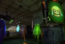 Three small, colorful, armless robot characters stand in a dim workshop looking at a screen displaying a creepy, distorted yellow face.