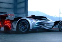 A sleek silver and black futuristic concept race car with glowing red taillights and aerodynamic styling parked outside an industrial building.