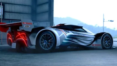 A sleek silver and black futuristic concept race car with glowing red taillights and aerodynamic styling parked outside an industrial building.