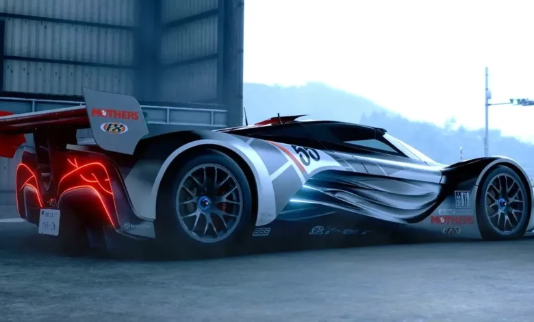 A sleek silver and black futuristic concept race car with glowing red taillights and aerodynamic styling parked outside an industrial building.