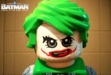 A close-up of a LEGO Joker minifigure with bright green hair and iconic smeared face paint from "LEGO Batman: Legacy of the Dark Knight."