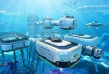A futuristic, modular underwater research base situated beneath a frozen ocean surface, surrounded by marine life and a large shark.