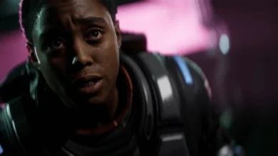 Close-up of Maria Rambeau in a futuristic suit looking on with a stunned expression against a glowing pink background.