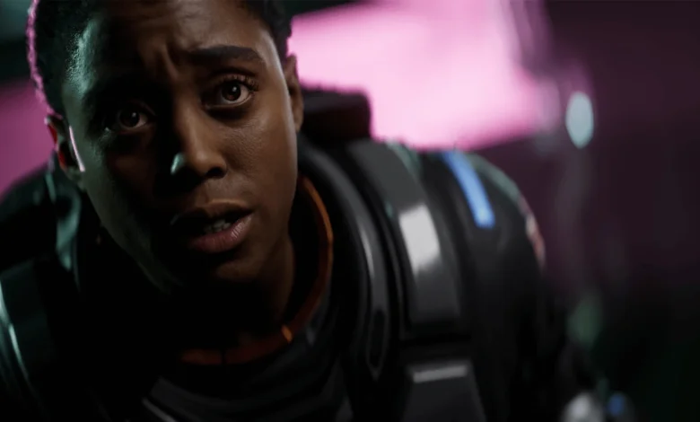 Close-up of Maria Rambeau in a futuristic suit looking on with a stunned expression against a glowing pink background.