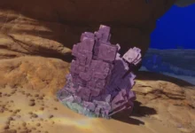 A large cluster of purple, cubic crystals sits on a sandy seabed beneath a rocky overhang.