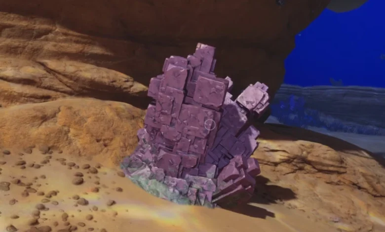 A large cluster of purple, cubic crystals sits on a sandy seabed beneath a rocky overhang.