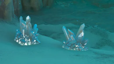 Two clusters of translucent blue crystals resting on the sandy floor of a dimly lit, bluish cavern.