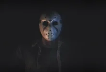 A figure wearing an iconic Jason Voorhees hockey mask emerging from deep shadows.
