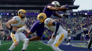 A Washington Huskies football player leaps to catch a pass over two Kent State defenders during a game in a crowded stadium.