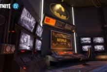 A high-tech Batcave command center in Fortnite featuring multiple surveillance monitors and a large yellow Batman logo on the wall.