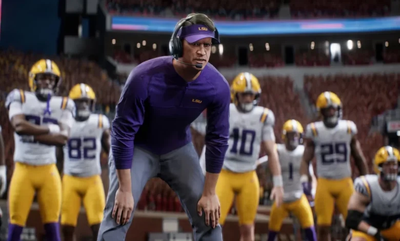 An LSU football coach wearing a headset and purple gear stands focused on the sideline with players in uniform behind him in a stadium.